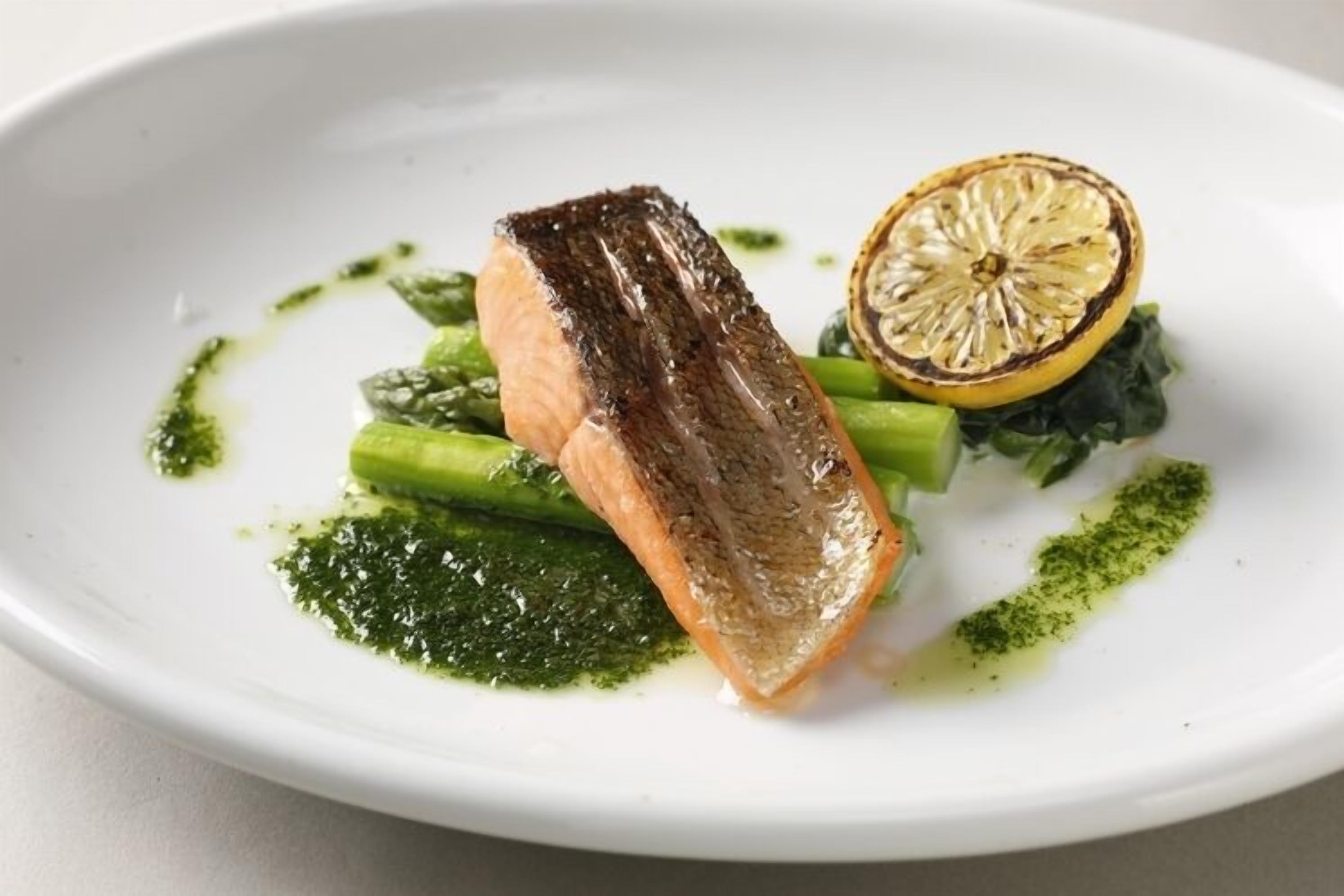 A white plate with a piece of salmon, broccoli, and a lemon half.