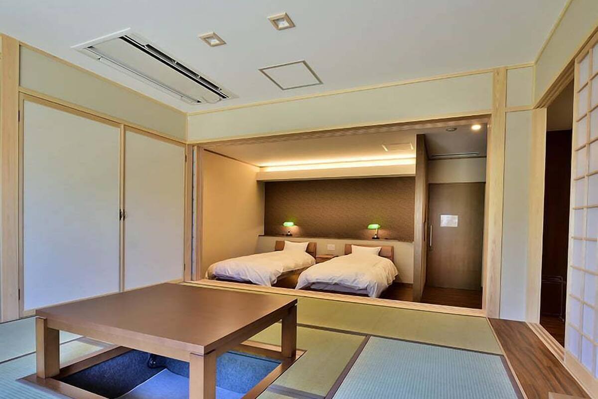 A traditional Japanese-style room with tatami flooring, a low wooden table, two beds with pillows, and a sliding door.