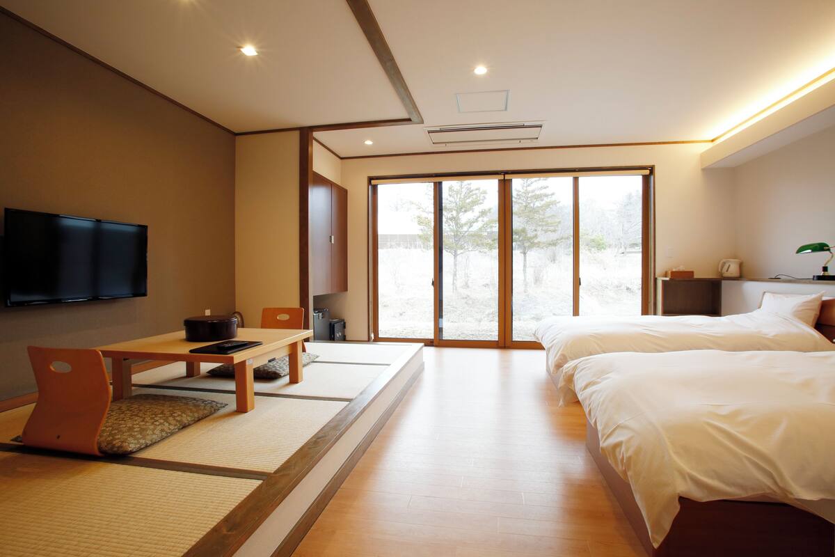 A hotel room with a bed, a desk, a chair, a television, and a sliding glass door leading to a balcony.