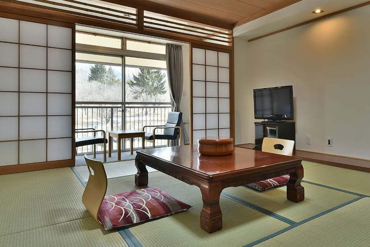 Une pièce de style japonais traditionnel, avec un sol recouvert de tatamis, une petite table en bois, un téléviseur et une vue sur l’extérieur.
