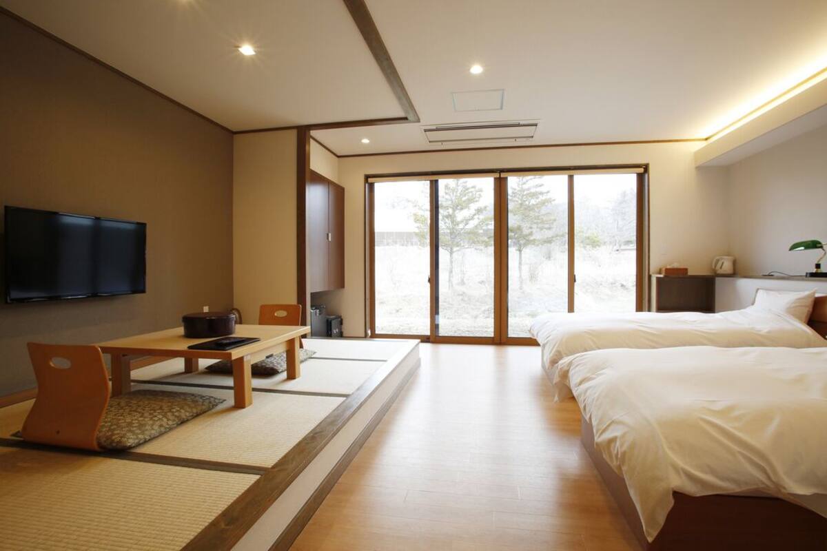 A modern hotel room with a bed, a desk, a television, and a sliding door leading to a balcony.