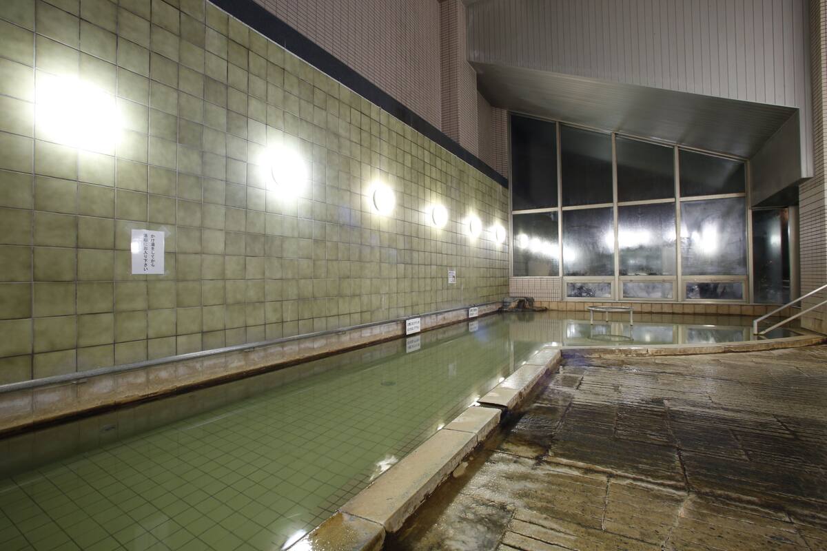 A swimming pool with tiled walls and a tiled floor, a window with a view, and a sign on the wall.