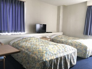 Habitación de hotel con dos camas, un escritorio, un televisor y una ventana con cortinas.