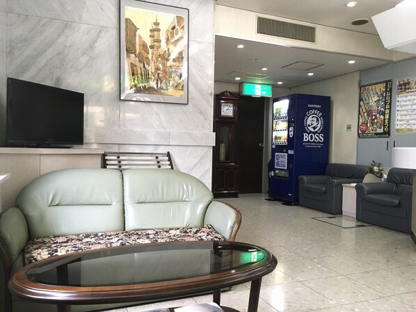 A lobby with a sofa, a glass-top table, a coffee vending machine, a clock, and a poster on the wall.