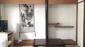 A traditional Japanese room with tatami flooring, a low wooden table, cushions, a TV, and a wall hanging. - Business Hotel Century (Iizuka)