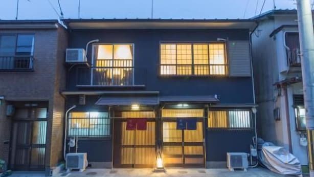 Un edificio de dos pisos con fachada oscura, ventanas grandes y una unidad de aire acondicionado visible.