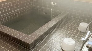 Una bañera de hidromasaje rectangular con revestimiento de azulejos, un grifo y dos dispensadores de papel higiénico en el suelo.