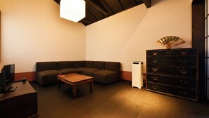 A room with a sectional sofa, a wooden coffee table, a television on a stand, a white cabinet, and a fan on a dresser. - Shibashi Umeyacho (Kyoto)