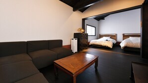 A room with a sofa, a wooden table, a dresser, and two beds. - Shibashi Umeyacho (Kyoto)