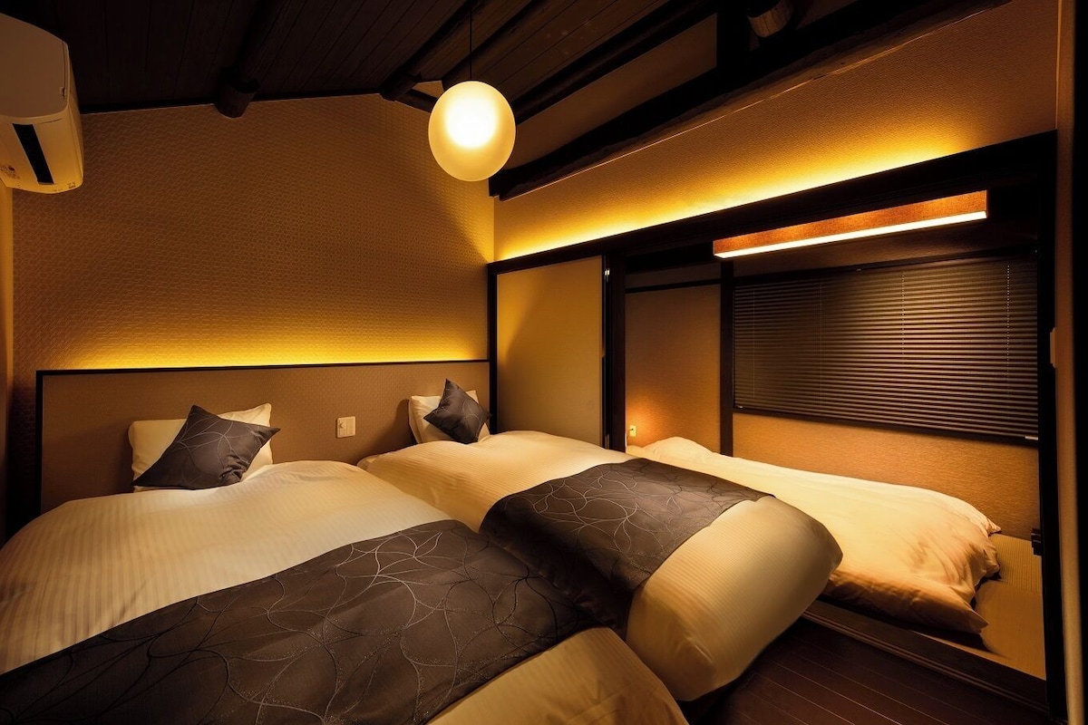 A hotel room with two beds, a ceiling fan, and a wall-mounted air conditioner.