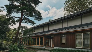 Un bâtiment moderne doté de grandes fenêtres et d’une façade en bois, entouré d’arbres et bordé d’un chemin de gravier.