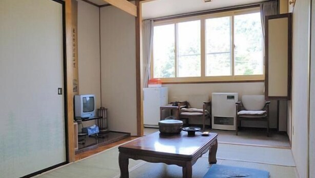 Una habitación japonesa tradicional con suelo de tatami, una mesa baja, un televisor y un calentador.