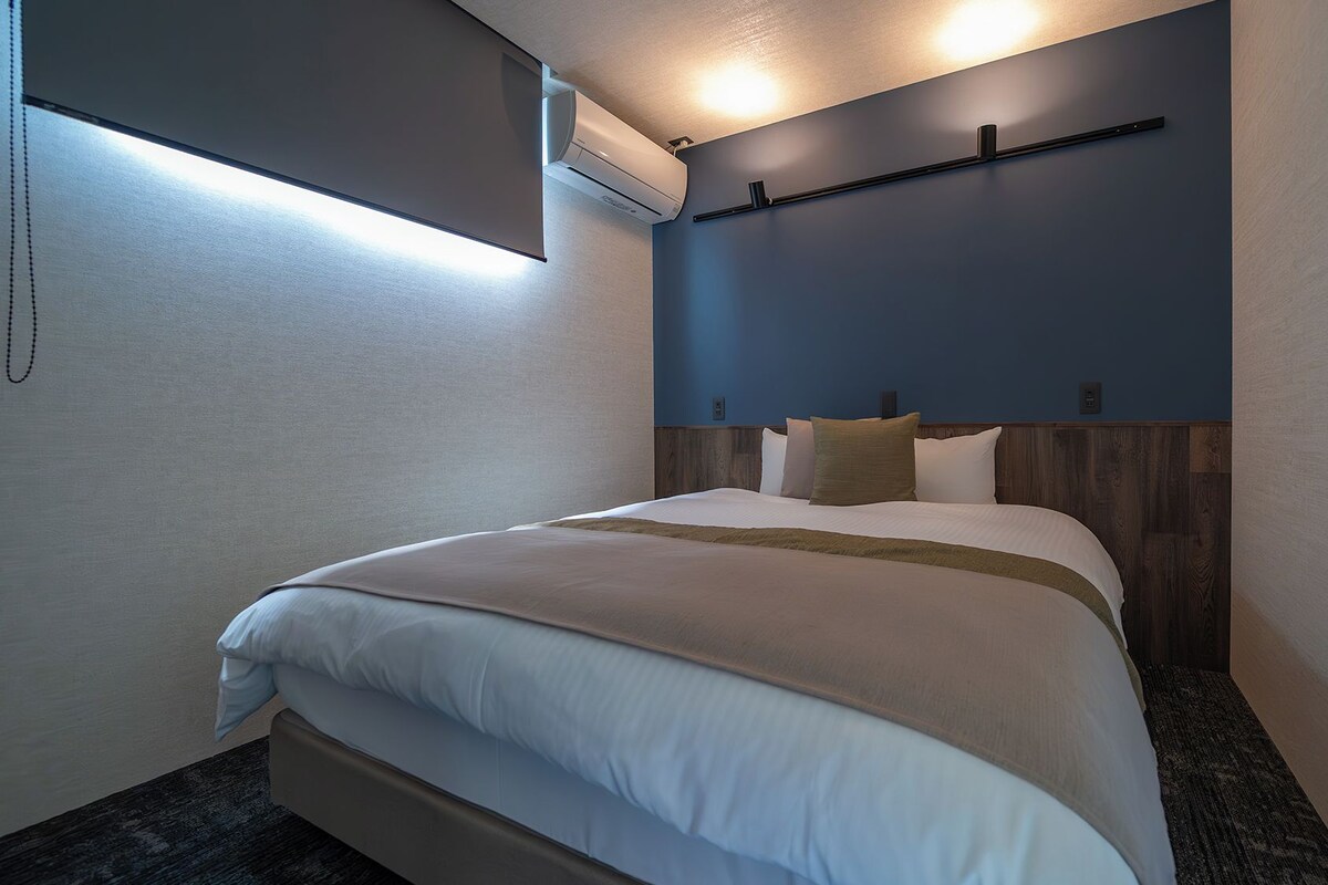 A hotel room with a bed, a wall-mounted air conditioner, and a ceiling light.
