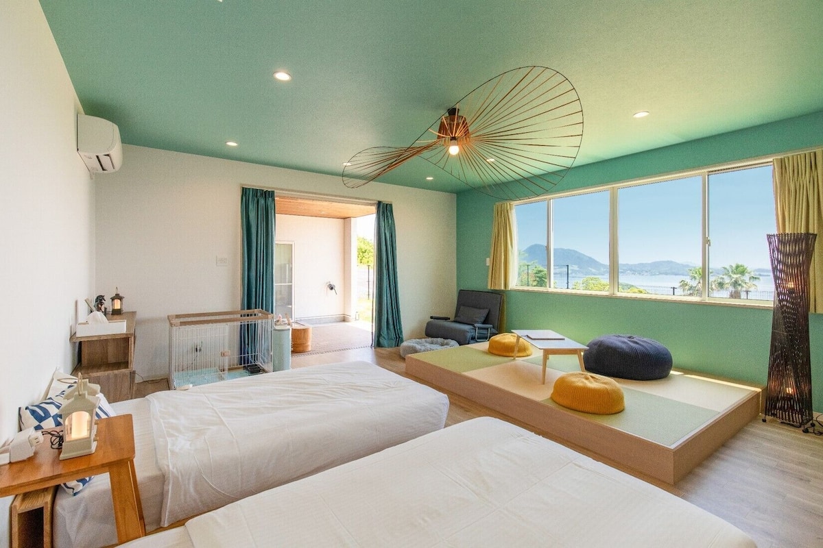 Quarto de hotel com duas camas, uma escrivaninha, uma cadeira, janela com vista e ventoinha no teto.