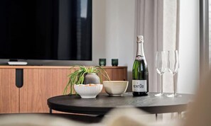 Un salón moderno con una televisión, una botella de vino y dos copas sobre una mesa.