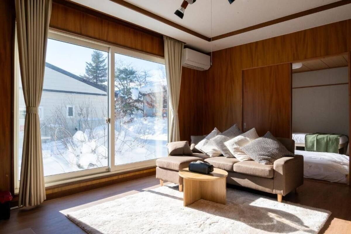 Ein gemütliches Wohnzimmer mit einer Couch, einem Couchtisch und einem großen Fenster mit Vorhängen.