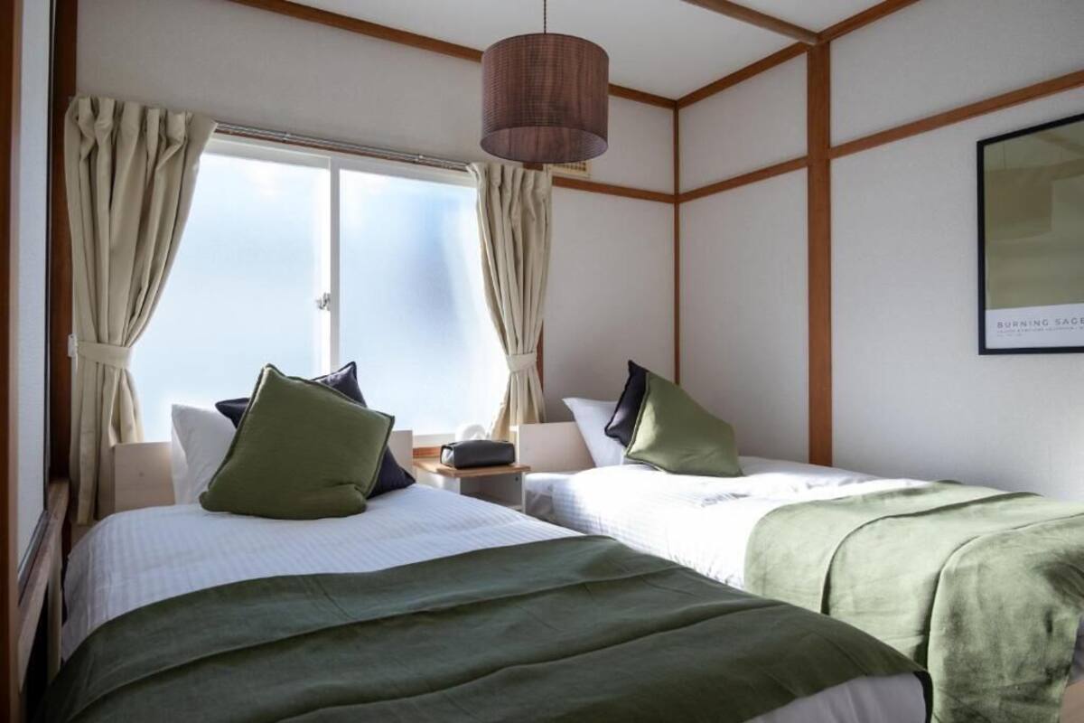 Ein Hotelzimmer mit zwei Betten, einem Vorhangfenster, einer Hängelampe und einem gerahmten Bild an der Wand.