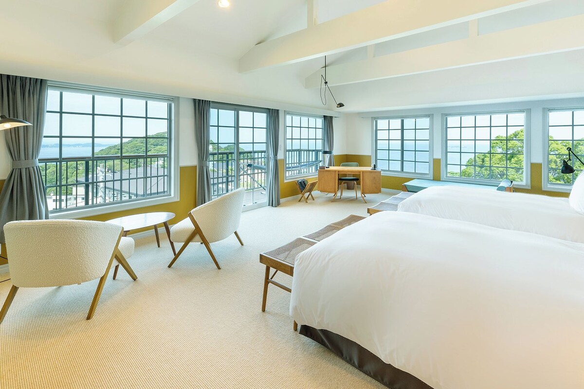 A hotel room with a large bed, a desk, a chair, and a view of the sea.