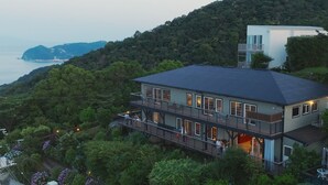 A multi-story house with a balcony, surrounded by lush greenery and overlooking a body of water. - Glamday Port Sea-view Hill (Atami)
