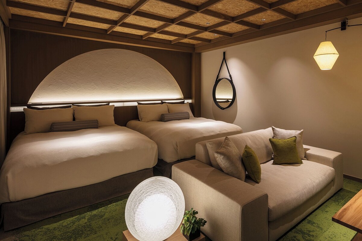 A hotel room with two beds, a sofa, a round table, and a lamp.