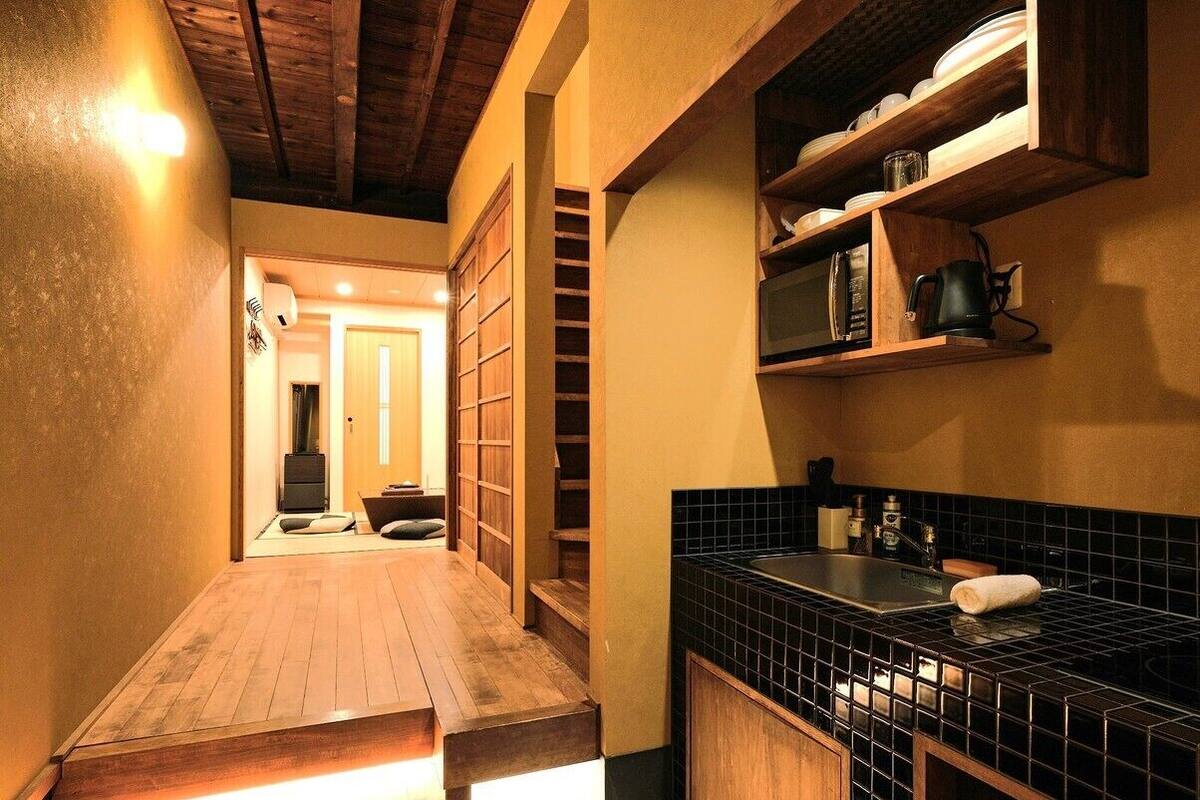 A narrow hallway leading to a bathroom with a wooden bench, a black tiled sink, and shelves with toiletries.