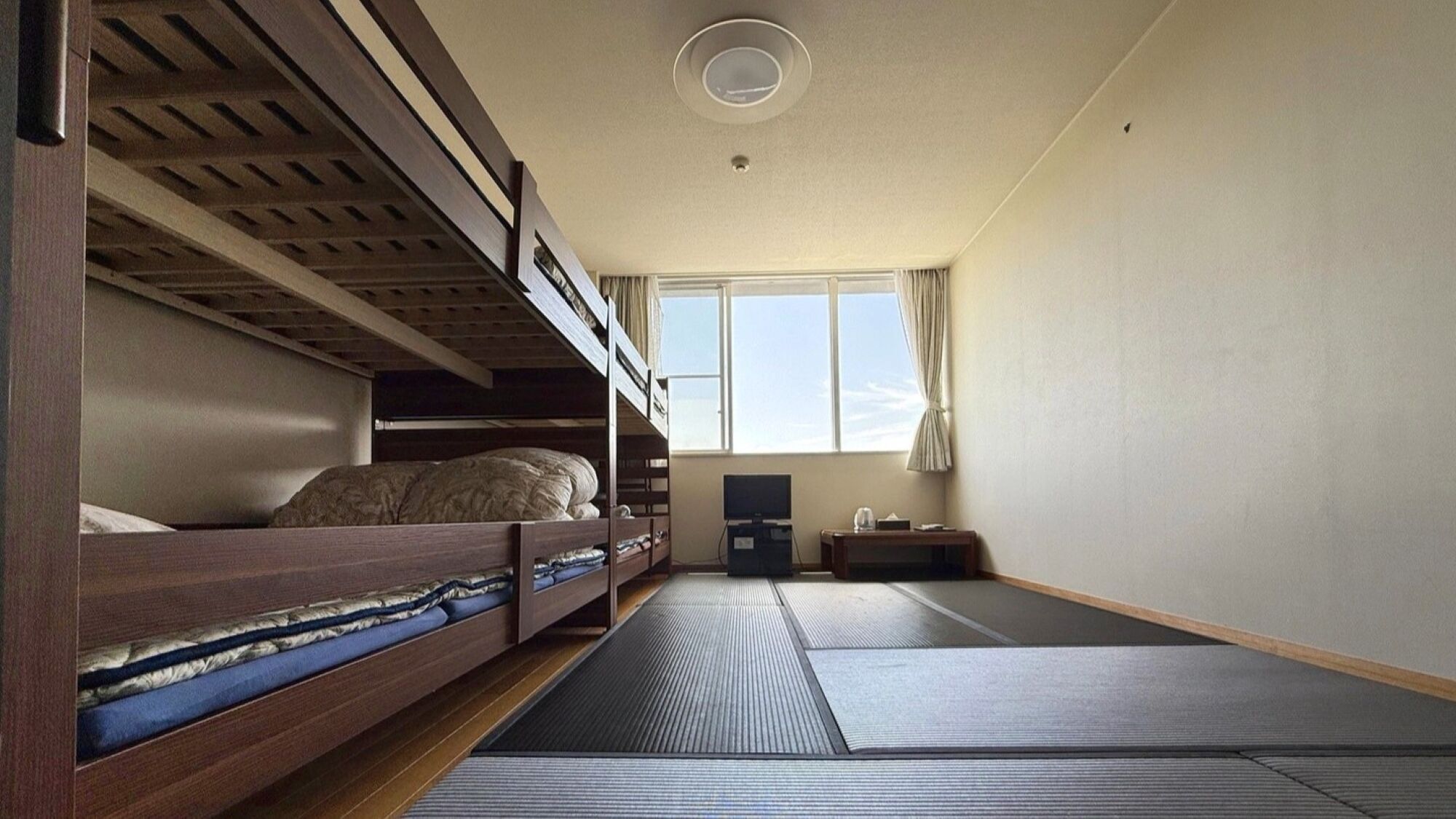Une chambre avec des lits superposés, une télévision, une petite table et une fenêtre avec des rideaux.