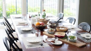 A dining table set with plates, cutlery, glasses, and bowls containing food and drinks, with a view of greenery outside. - Glampetit Koh (Atami)