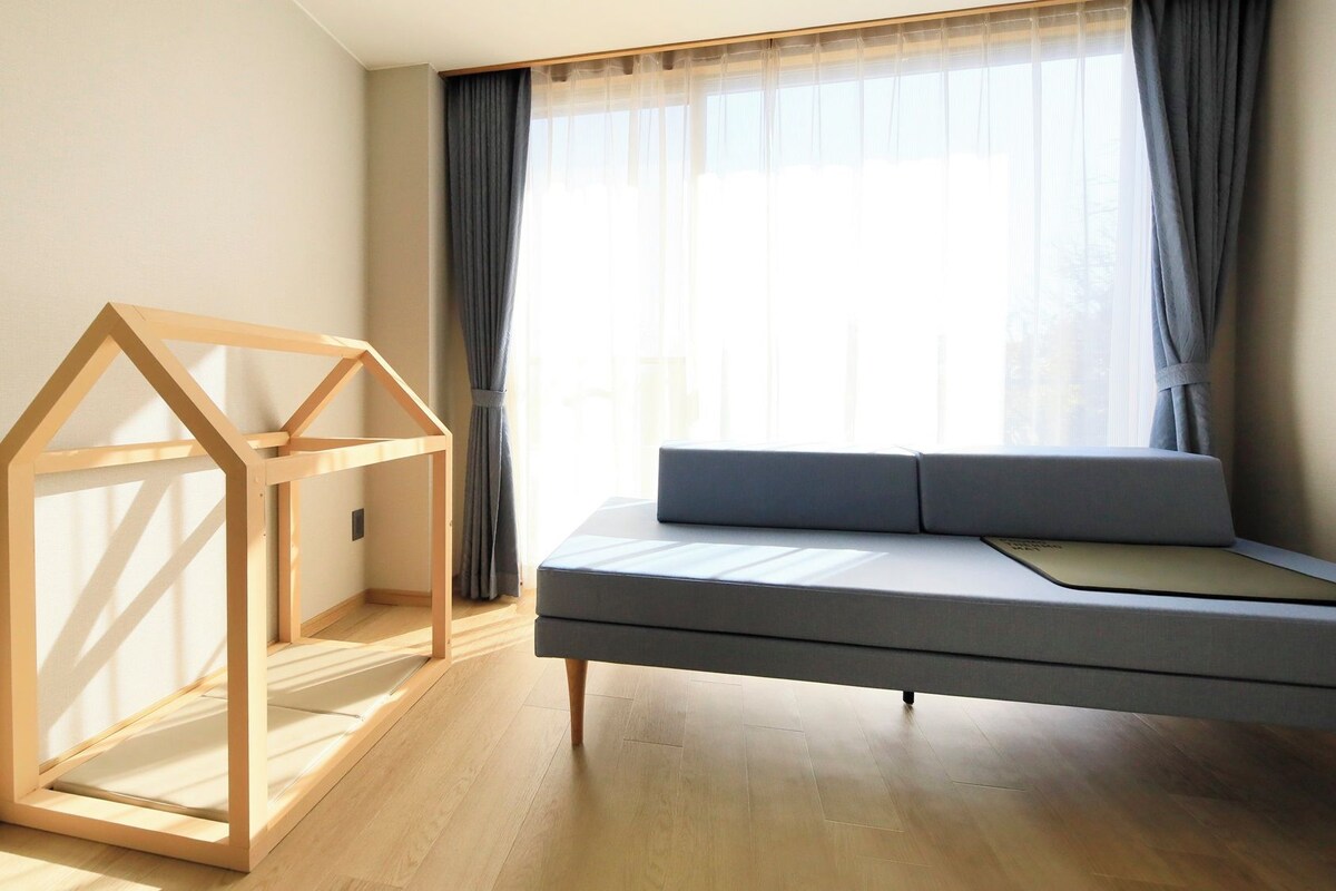 A room with a wooden bed frame, a sofa, and a window with curtains.