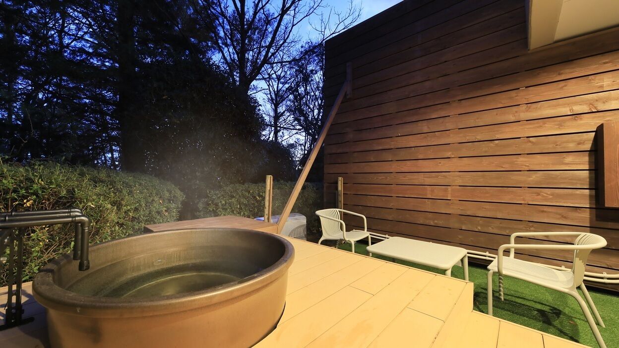 A wooden deck with a hot tub, outdoor furniture, and a wooden wall.