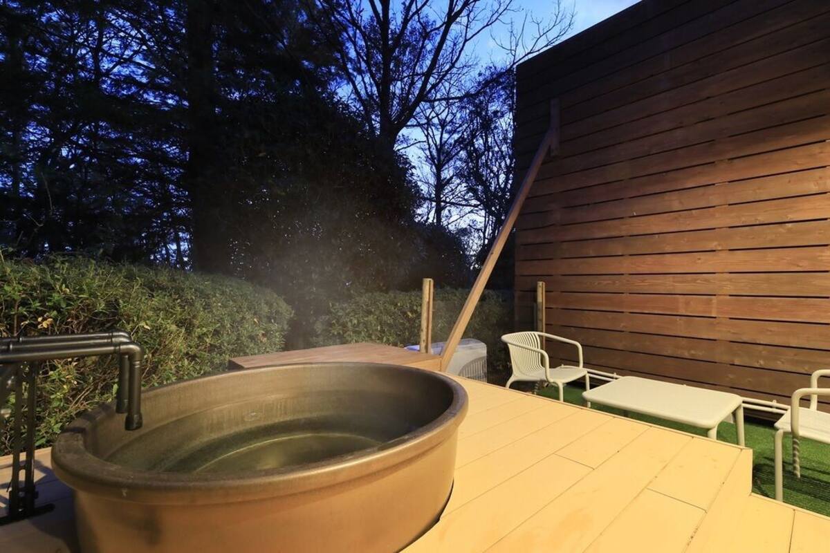 Una terraza de madera con jacuzzi, mobiliario exterior y un muro de madera.