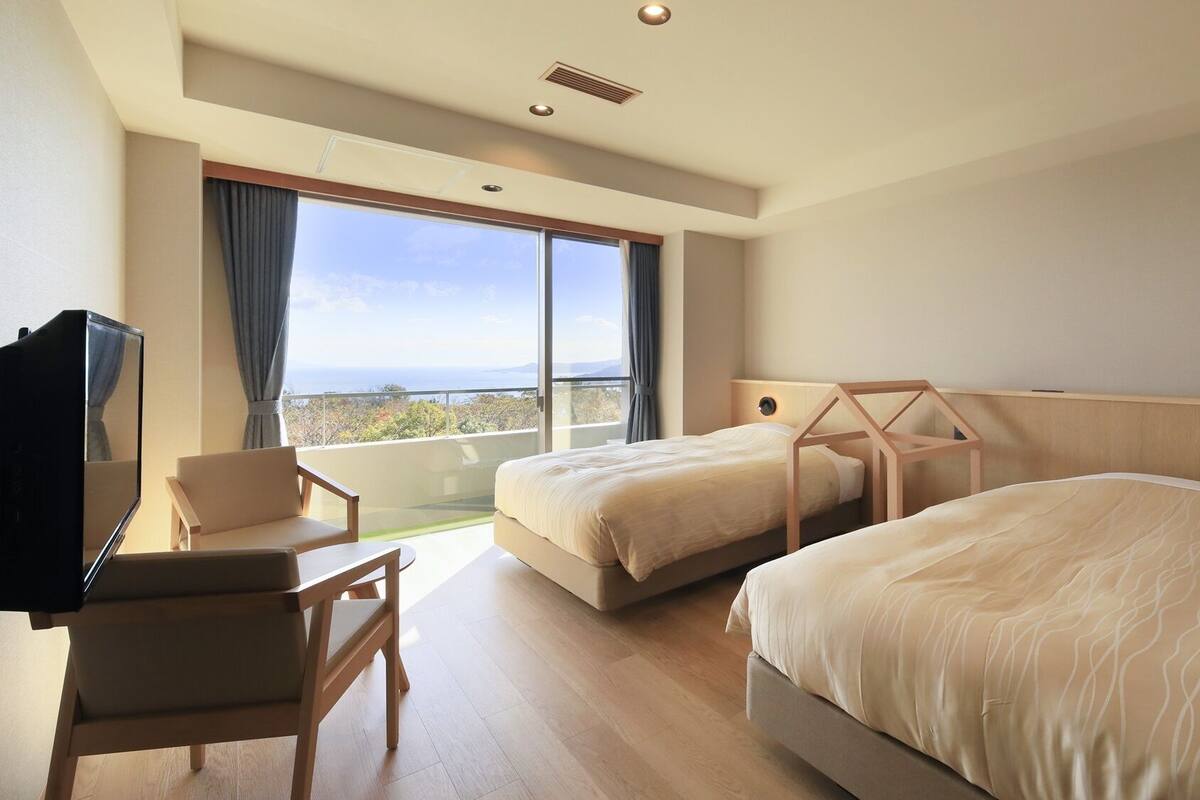 Una habitación de hotel con dos camas, un escritorio, una silla y un ventanal con vistas.