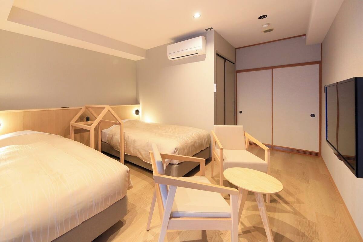 Habitación de hotel con dos camas, una silla, una mesita, aire acondicionado y un televisor.