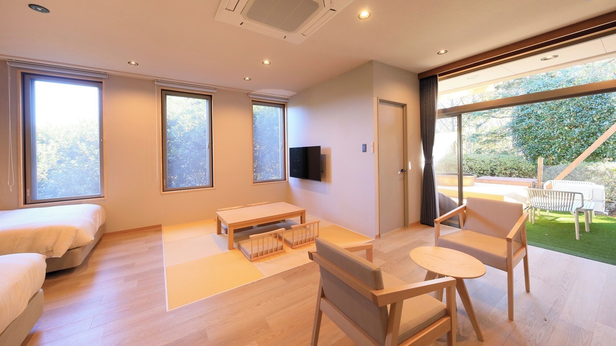 A modern living room with a sofa, a table, a TV, and large windows.