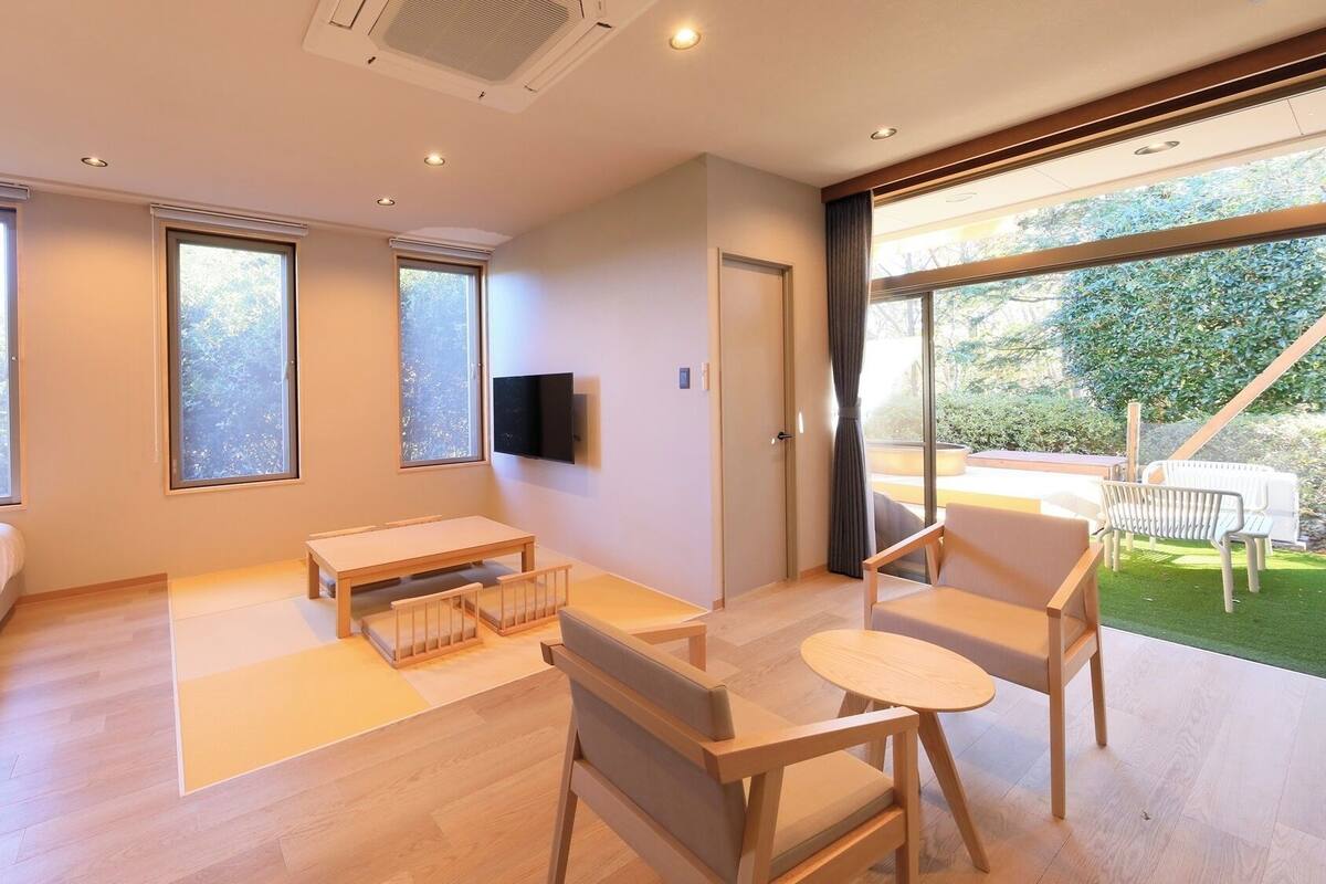 Una sala de estar moderna con sofá, mesa, televisor y ventanas amplias.