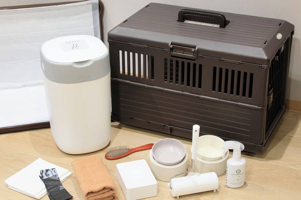 Un estuche de viaje con asa, un recipiente cilíndrico blanco, un estuche marrón con ranuras de ventilación, un cepillo para el cabello, una toalla, una caja blanca, un bol, una taza y una botella.