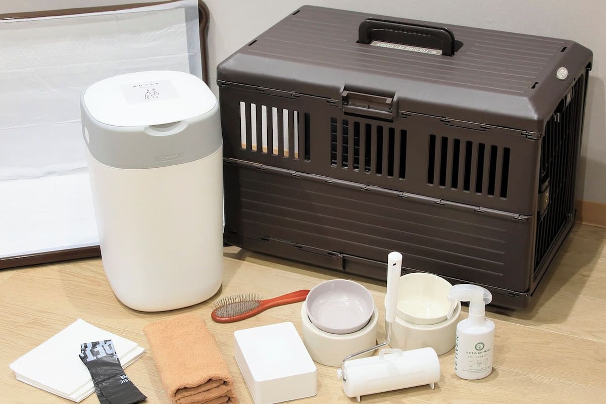 A travel case with a handle, a white cylindrical container, a brown case with ventilation slits, a hairbrush, a towel, a white box, a bowl, a cup, and a bottle.