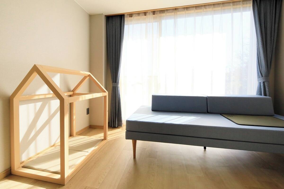 Una habitación con estructura de cama de madera, un sofá y una ventana con cortinas.