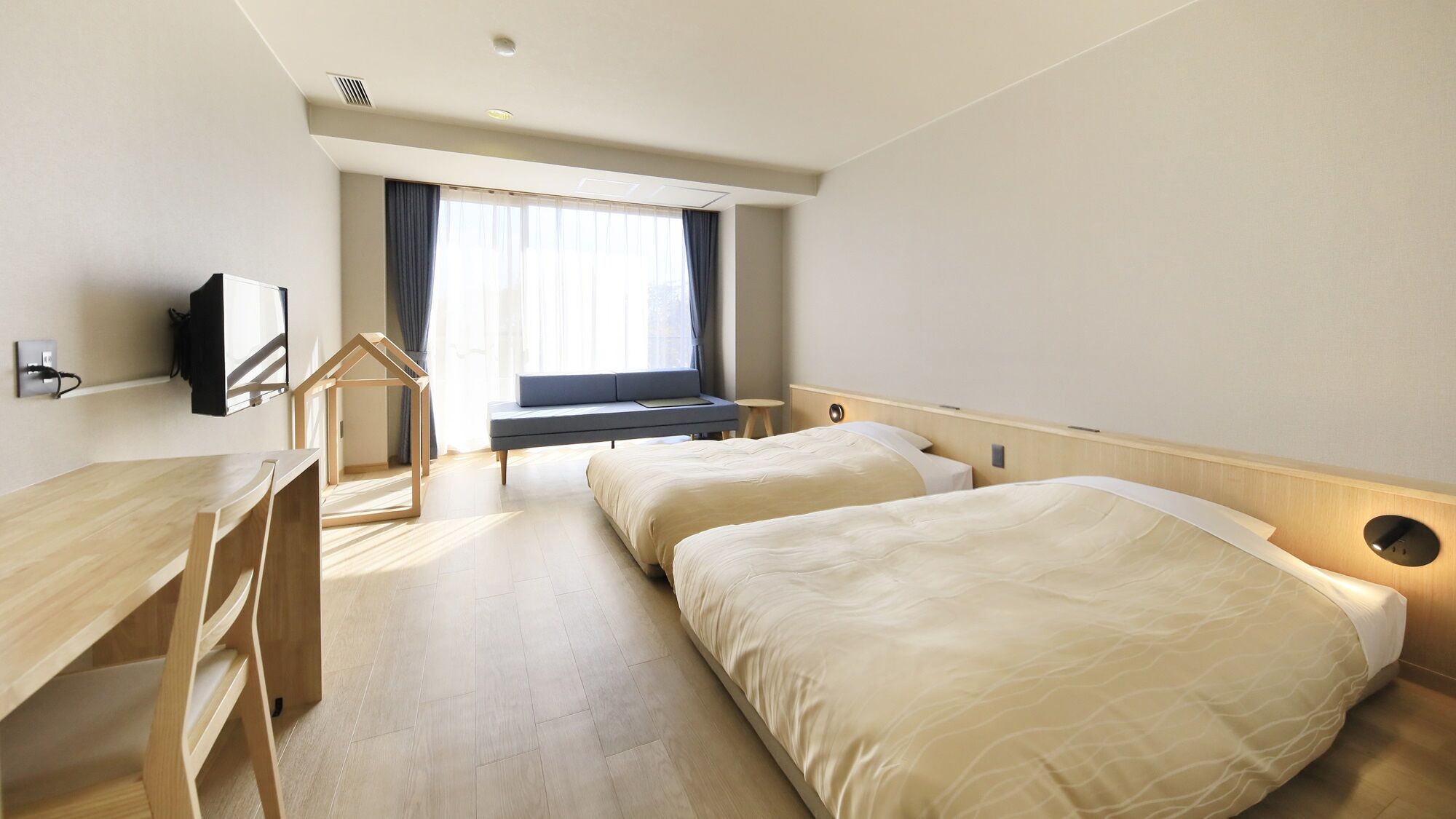 A hotel room with a desk, two beds, a TV, and a window with curtains.
