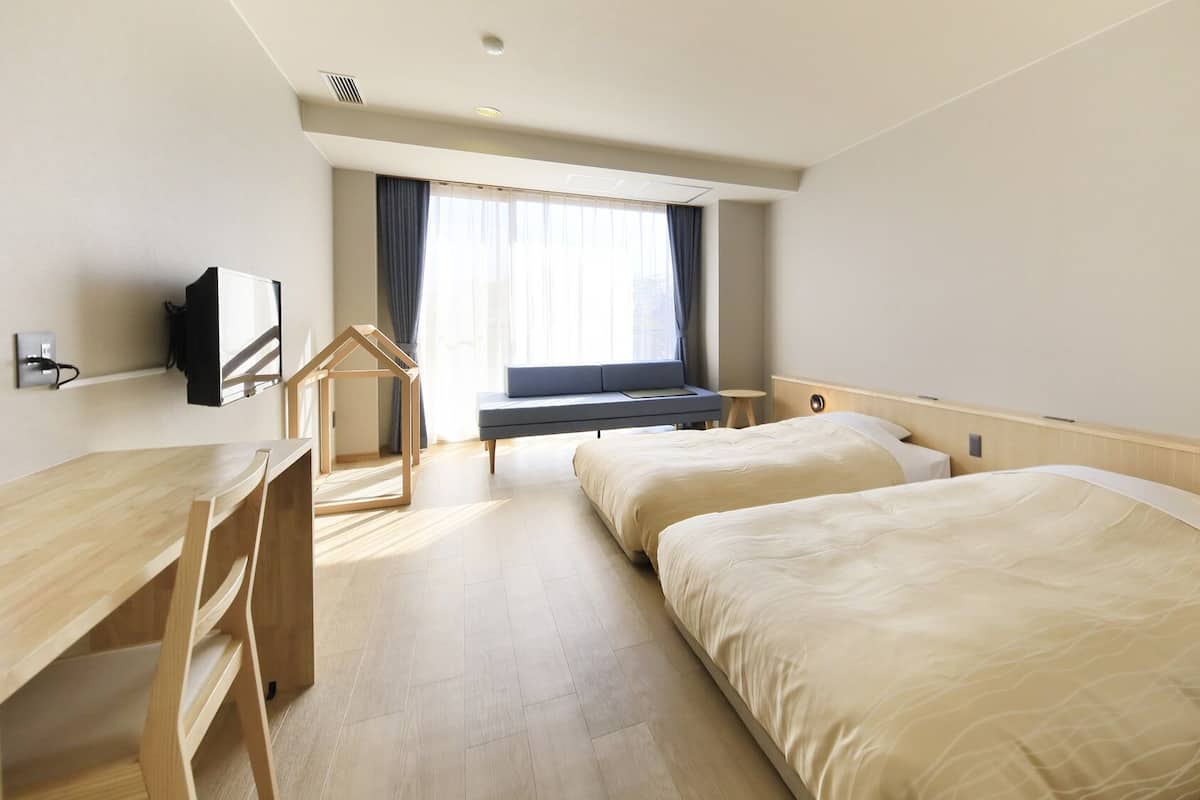 Habitación de hotel con escritorio, dos camas, televisor y ventana con cortinas.