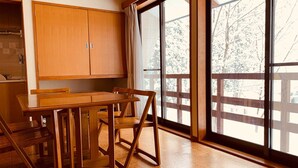 Een keuken met houten kastjes, een eettafel en stoelen, en grote ramen met uitzicht op bomen.