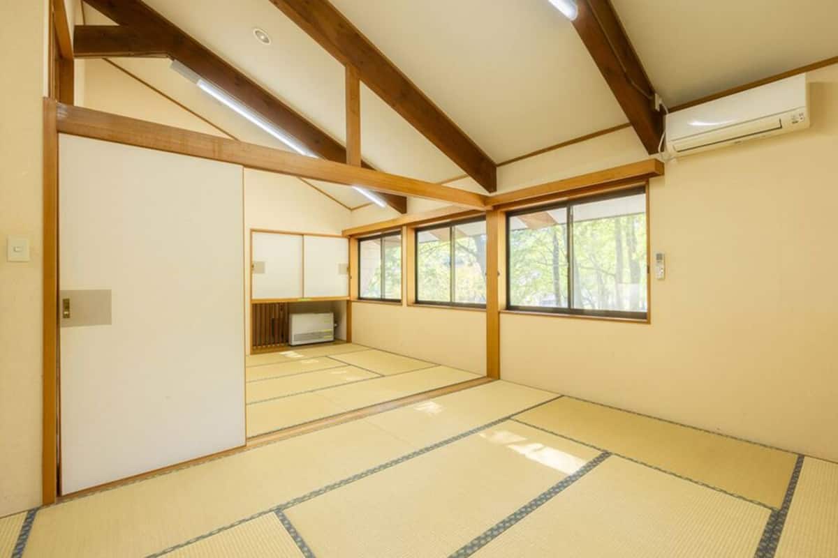 Ein traditioneller japanischer Raum mit Tatami-Böden, Holzbalken, einem Fernseher und großen Fenstern.