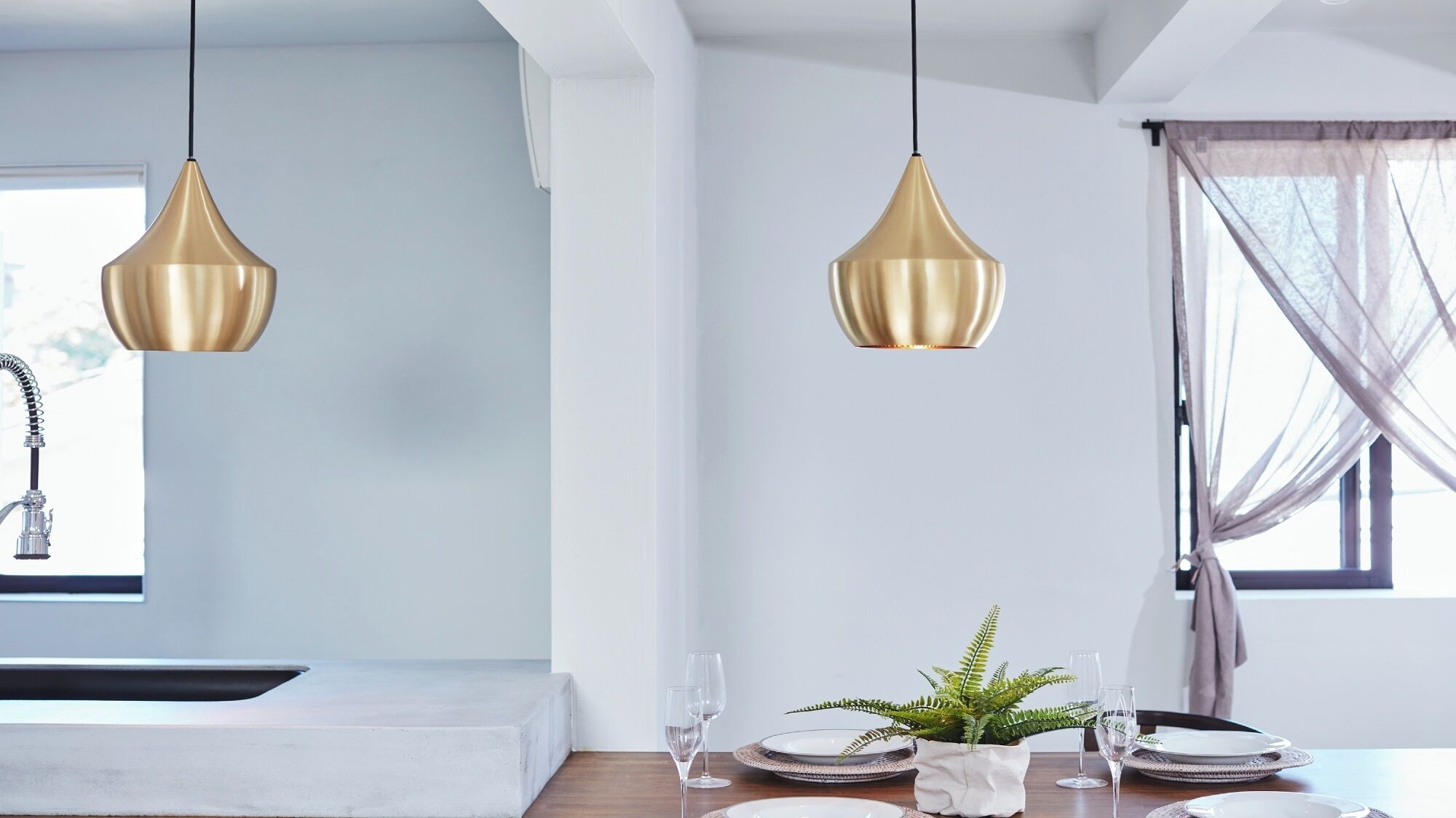 A modern kitchen with pendant lights, a sink, and a dining area with a plant and tableware.