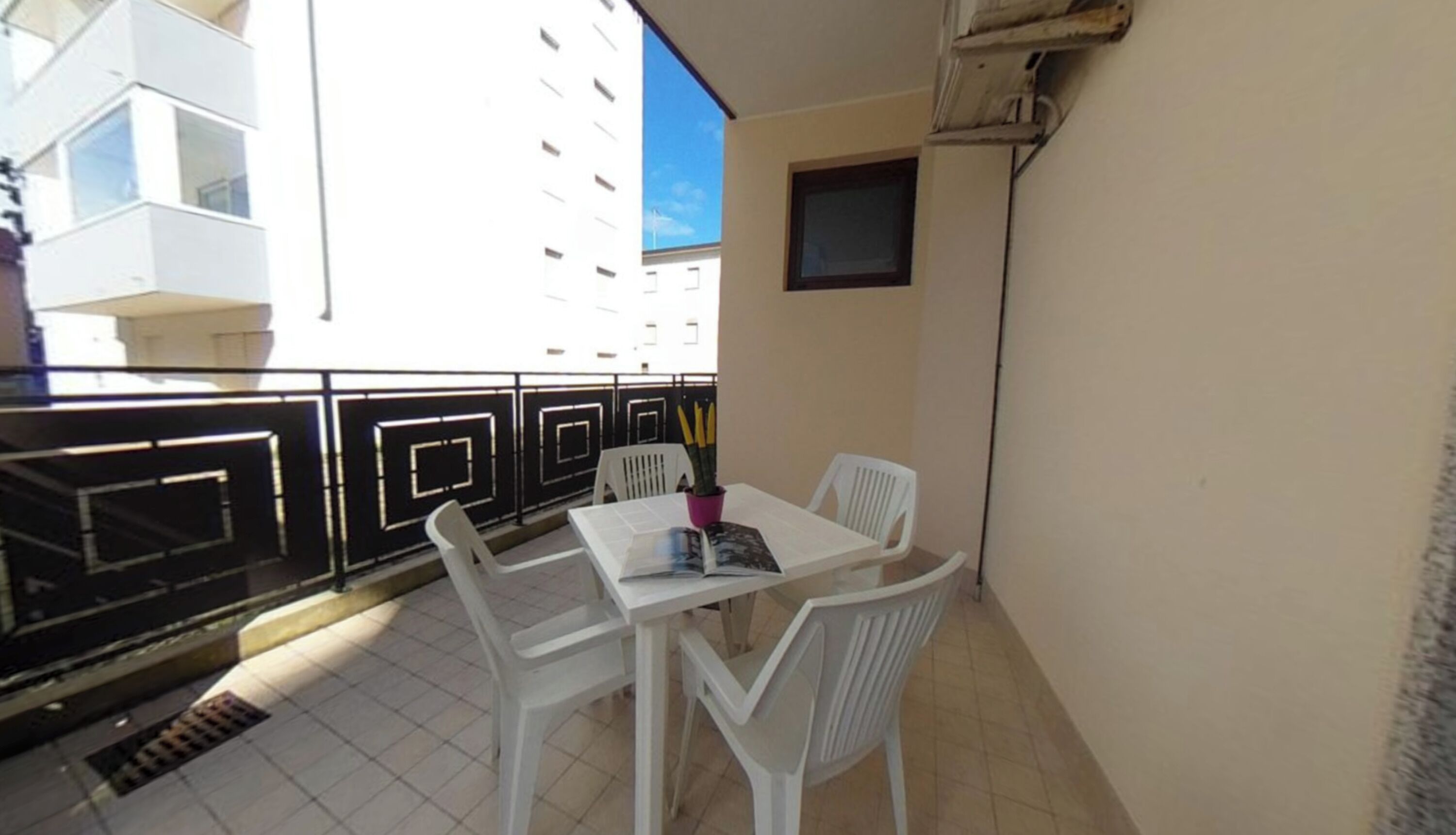 A balcony with a table and chairs, a potted plant, and a view of a building.