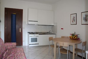 A compact kitchen with white cabinets, a stove, and a dining table with chairs. - Inviting Apartment in a Great Area (Lignano Sabbiadoro)