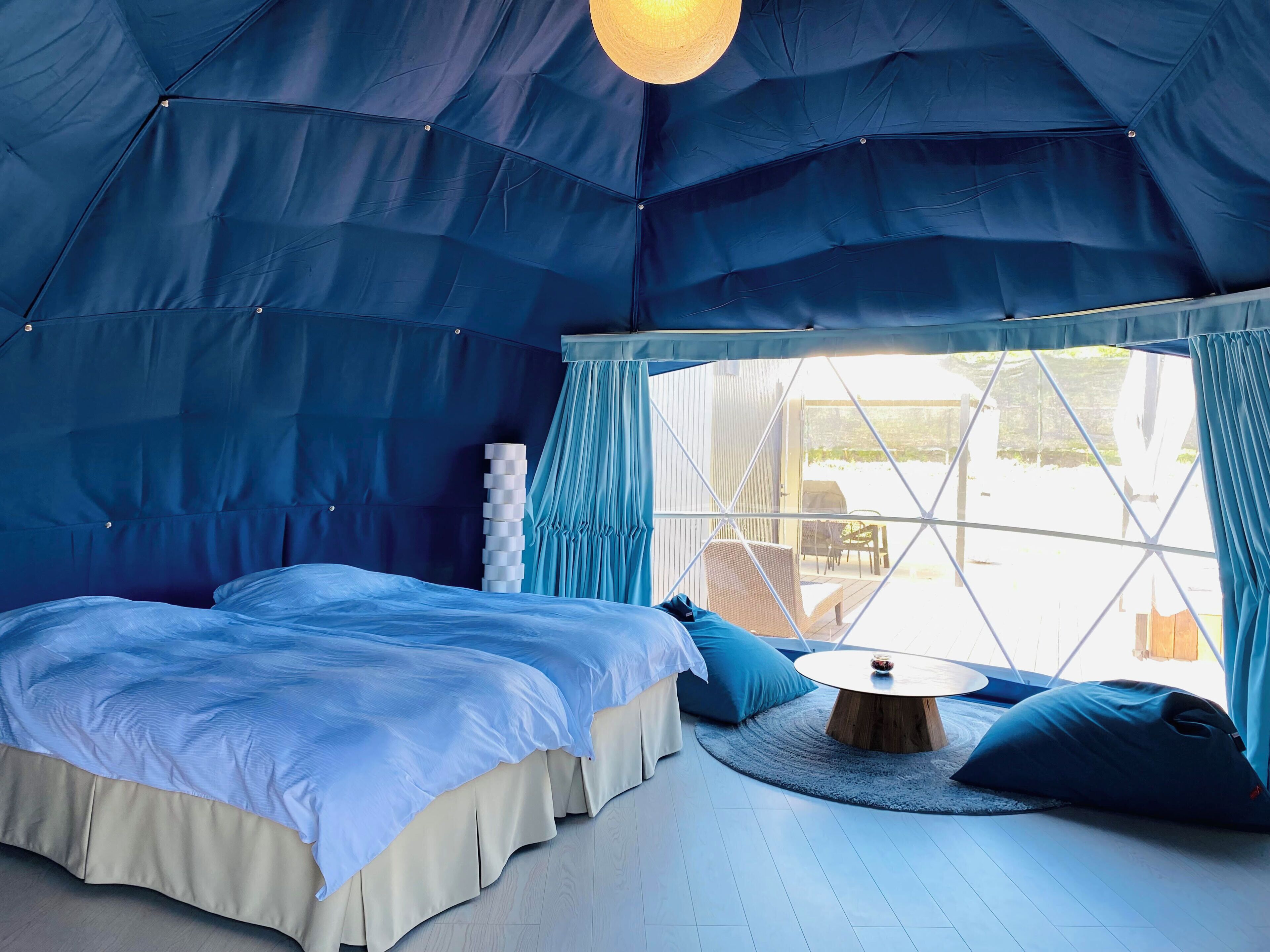 Um quarto tipo tenda com uma cama, uma mesa redonda e vista através de uma grande janela.