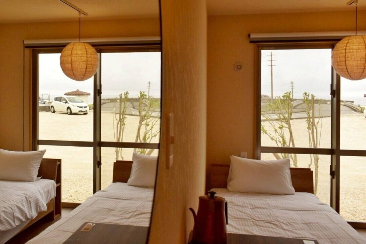 Quarto com duas camas, janelas amplas e vista para um estacionamento e para a praia.