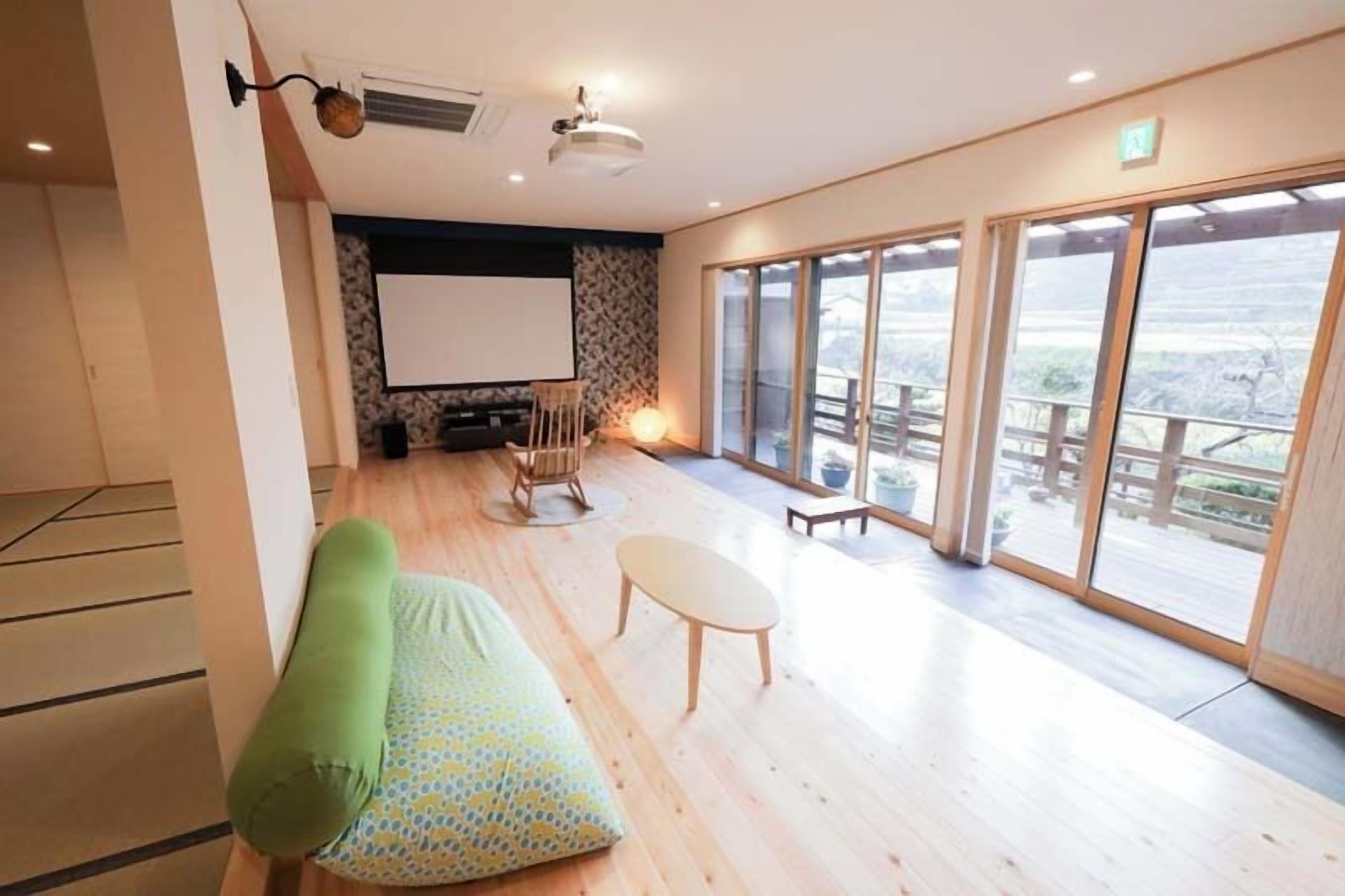 A room with a sofa, a small table, a projector screen, and large windows.