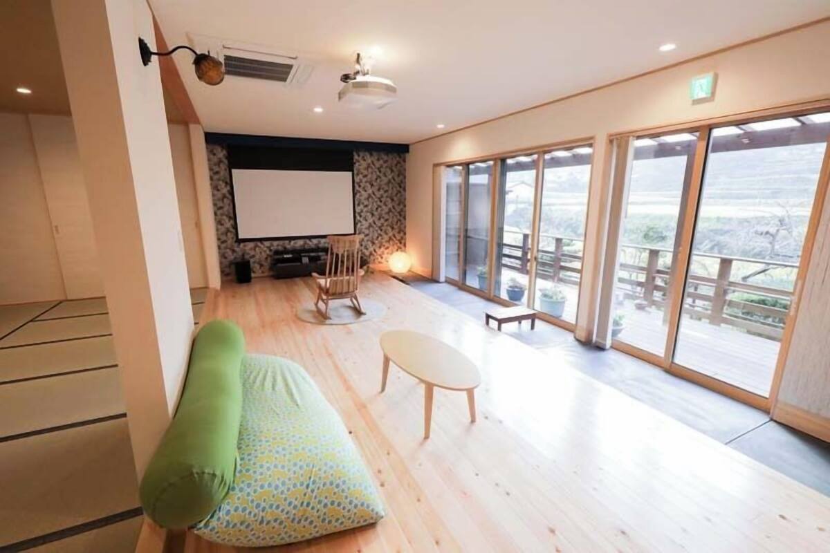 A room with a sofa, a small table, a projector screen, and large windows.