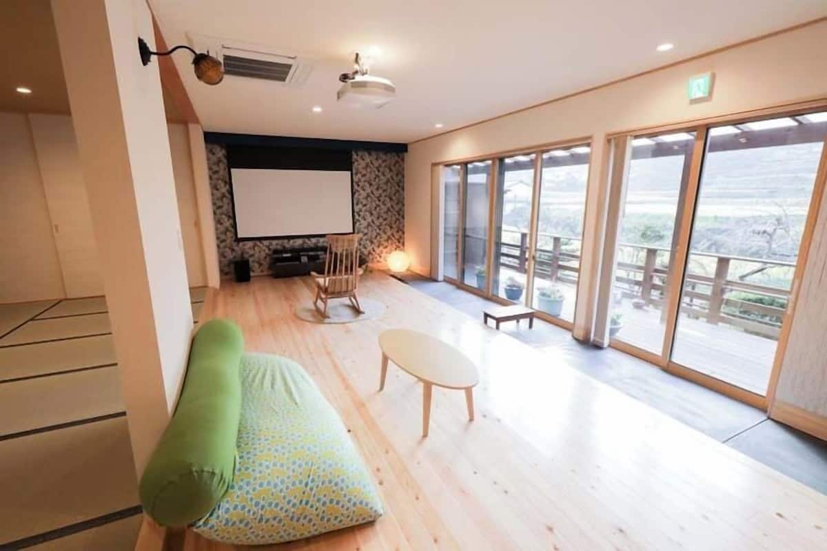 A room with a sofa, a small table, a projector screen, and large windows.