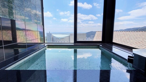 A modern indoor swimming pool with large windows offering a view of buildings and hills. - Glampetit Horizon (Atami)